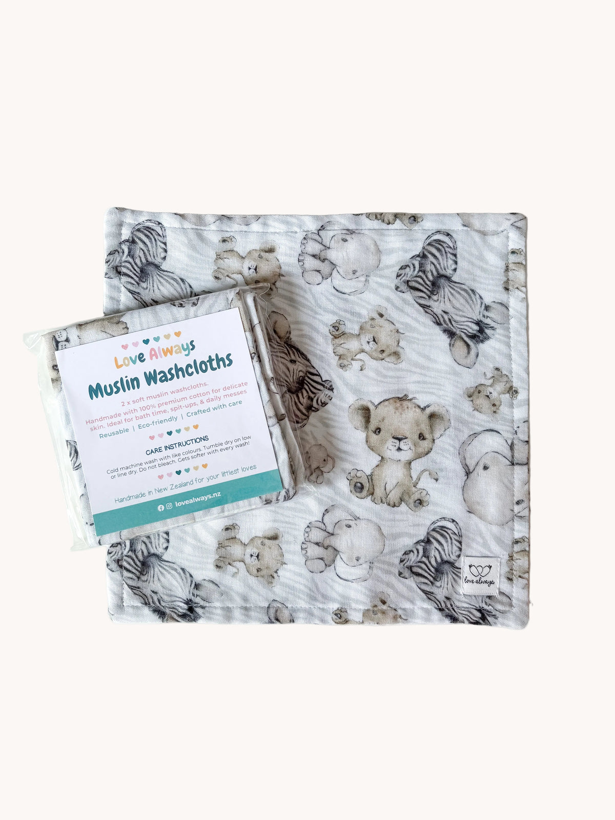 The Little Safari muslin washcloth laid flat with its packaged set resting on top — grey and cream lion cubs, elephants, zebras and hippos on a soft white muslin square