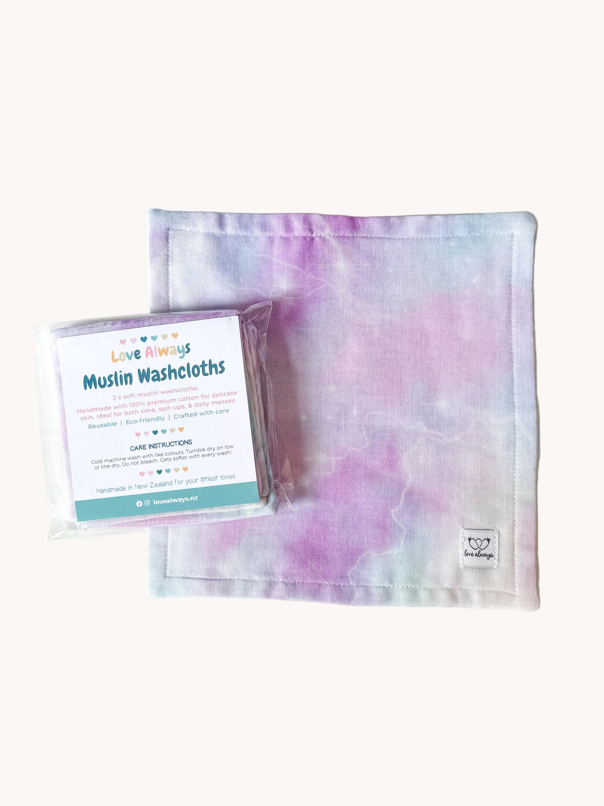 The Cosmic Whisper muslin washcloth laid flat with its packaged set resting on top — soft lilac and mint watercolour clouds on a white muslin square