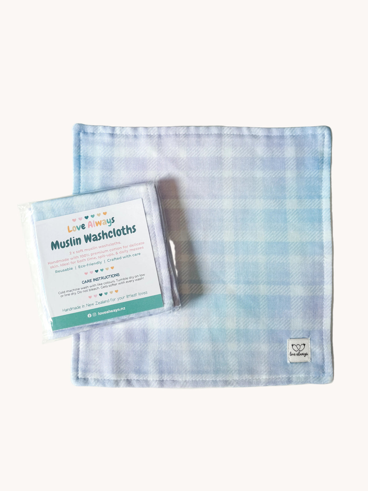 The Rainbow Gingham #2 muslin washcloth laid flat with its packaged set resting on top — pale blue gingham check on a soft white muslin square