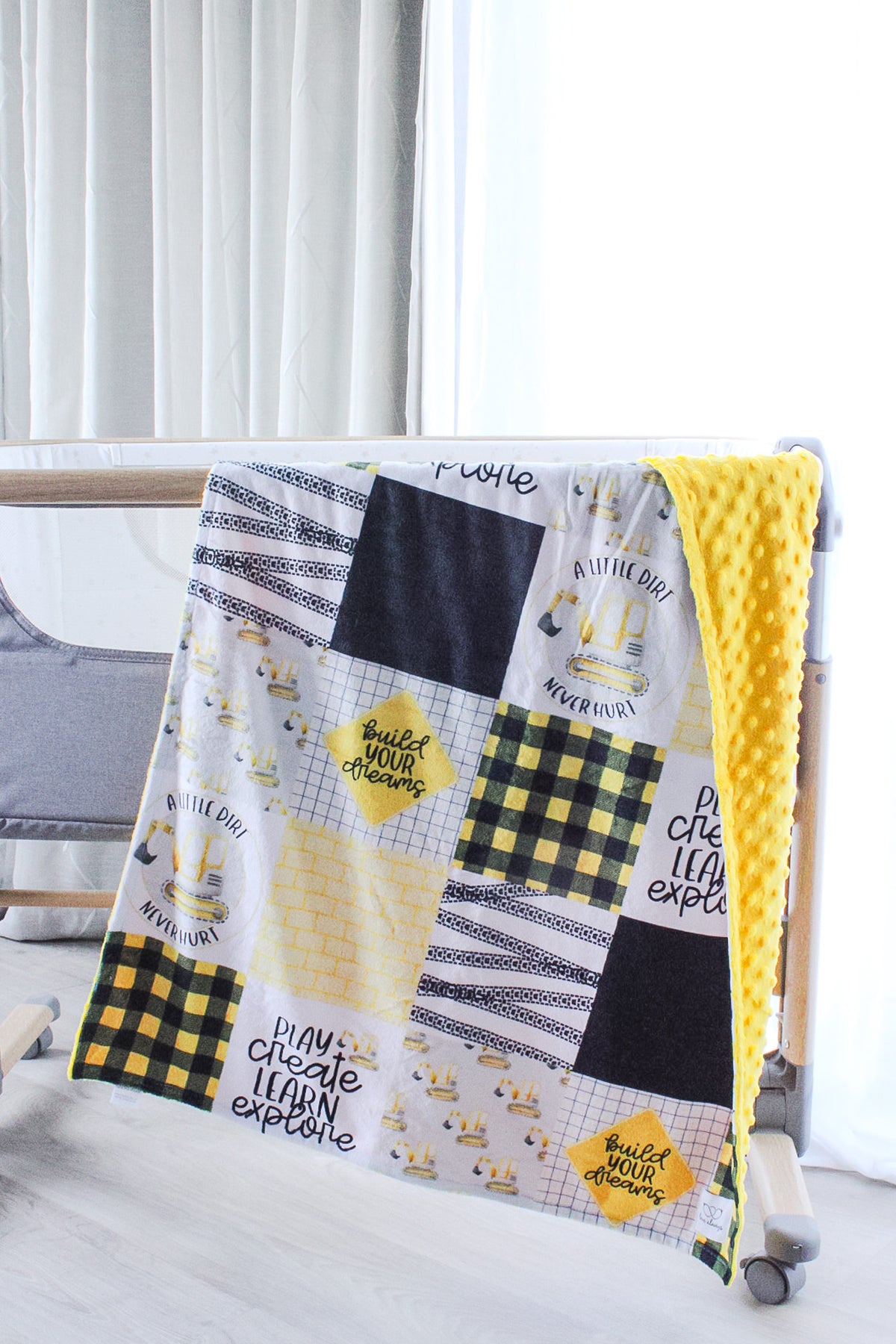 The Build Your Dreams Yellow minky blanket hanging over a bassinet rail with one corner folded back to show the yellow dimpled backing