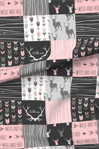 Little Hunter Baby Pink minky fabric — patchwork squares of stag silhouettes, deer, arrows and wood grain in charcoal, soft pink and grey, with antlers around the words little one and bands reading wild and free