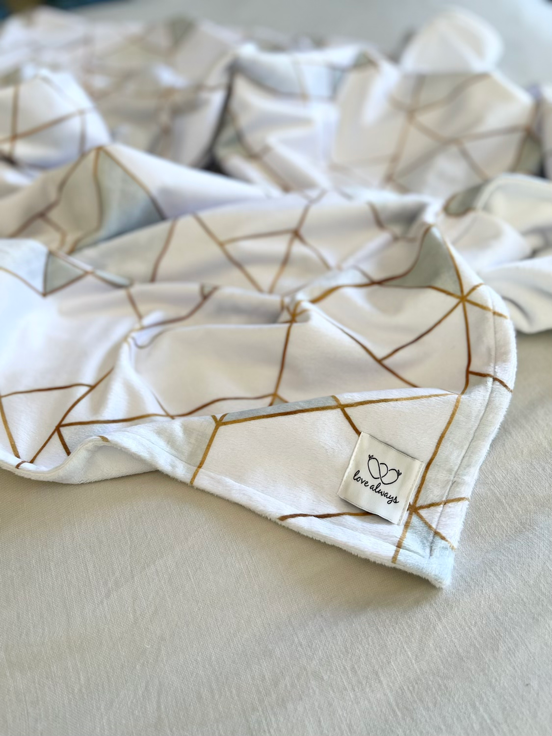Close-up of the Geometric Triangles White and Gold minky blanket corner, showing the gold triangles and the Love Always label